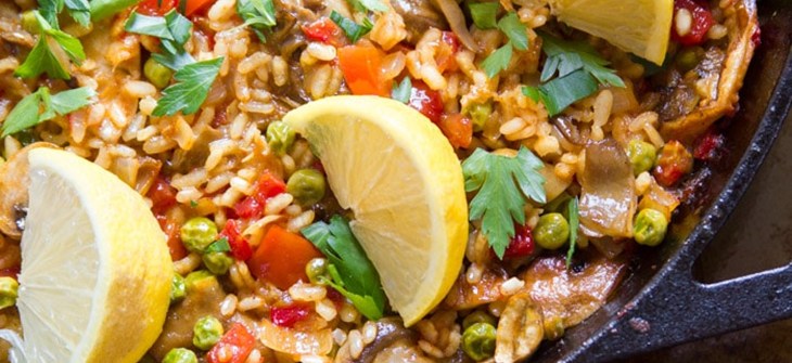 Cast iron pan filled with mushroom paella and topped with three lemon wedges.