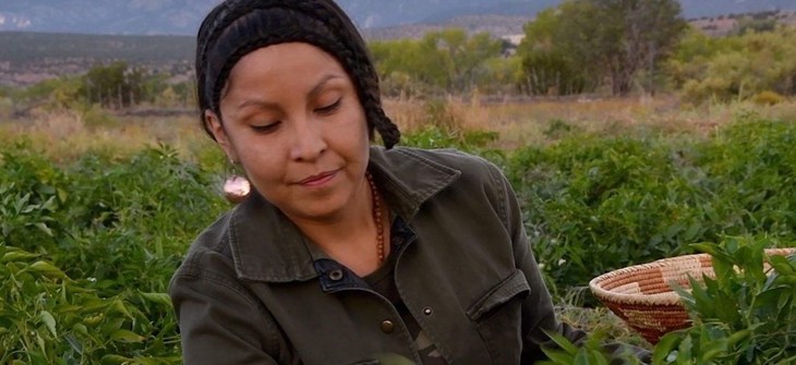 Tina stands in a field tending to crops in a green jacket