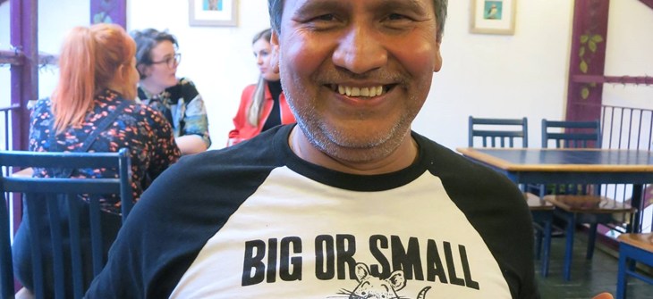 Gerardo stands facing the camera in a black and white baseball t-shirt with the image of a chicken and a cow which reads "Big or Small".