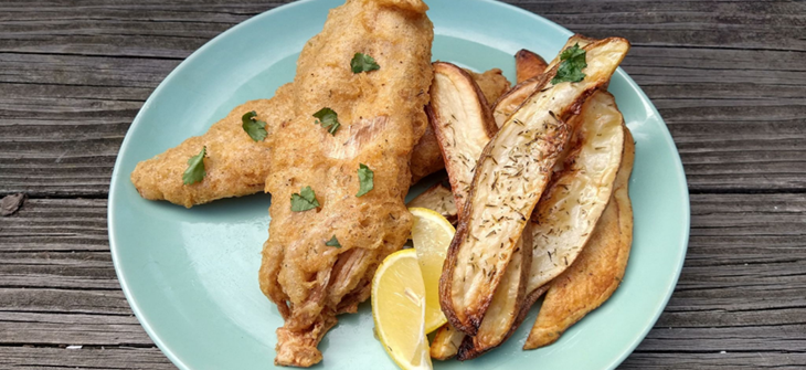 Homemade version of original recipe: Bana Blossom fish and chips sit on sea green plate on wood grain background with a lemon wedge
