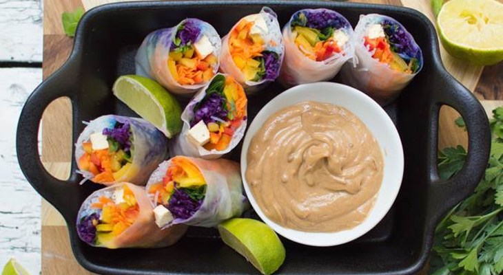 Spring rolls sitting next to cast iron pot of peanut sauce