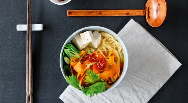 Miso soup in a white bowl with a wooden ladle laying horizontally above the bowl