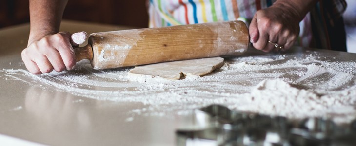 hands on a rolling pin flattening a disk of dough onto a white counter top