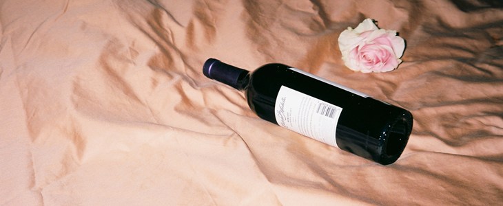 Unopened bottle of wine laying on a bed with pink sheets