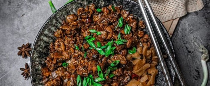 on a black slate background in a black bowl sits a bed of rice on a soy drizzled tempe grounds