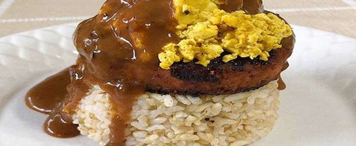 On a white plate is a stack of rice topped with a plant-based patty and a yellow tofu scramble