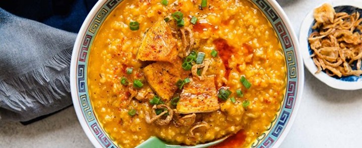 On a white table in a white bowl is bright orange millet with vegetables