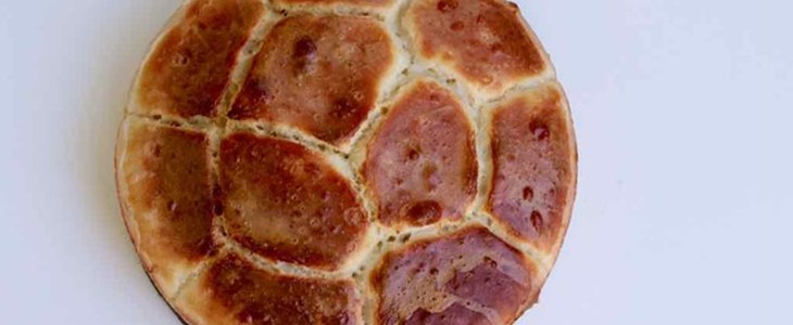 On a white background a tin of pull apart bread with a criss-crossed pattern sits with a golden crust