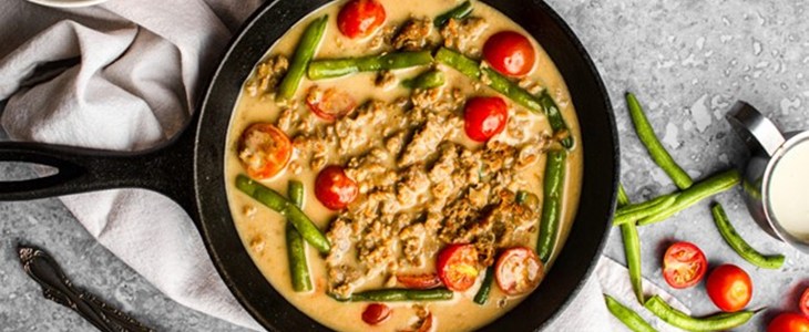 on a grey speckled table surrounded by cast iron pots is a white bowl filled with rice and plant based crumbles in a yellow coconut milk broth