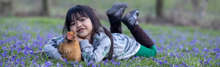 girl holding a hen while lying on a bed of flowers