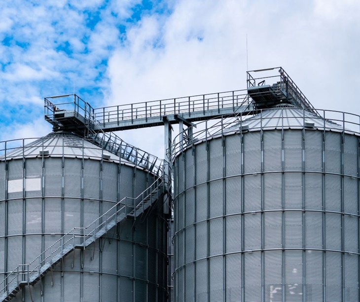 Two large industrial agricultural silos stand high with a blue sky peppered with clouds.